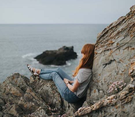 Woman sits on rocks overlooking ocean.