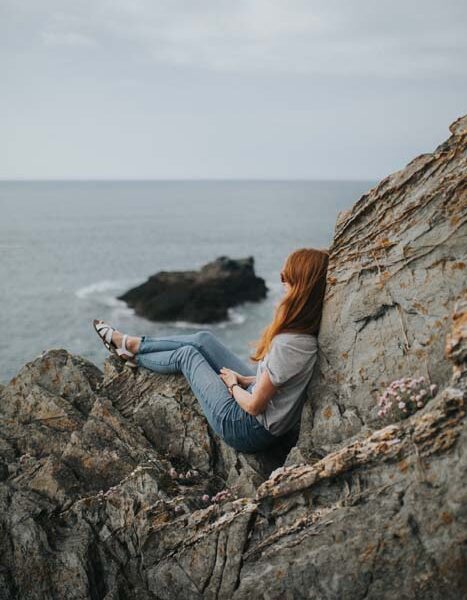 Woman sits on rocks overlooking ocean.
