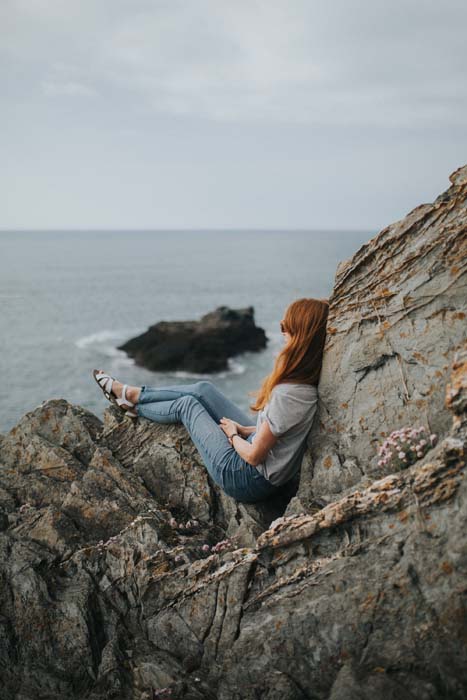 Woman sits on rocks overlooking ocean.