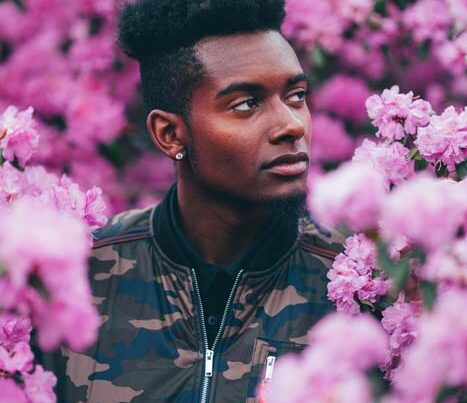 Man in camo jacket amidst pink flowers.