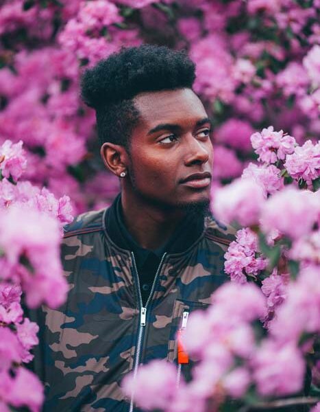 Man in camo jacket amidst pink flowers.