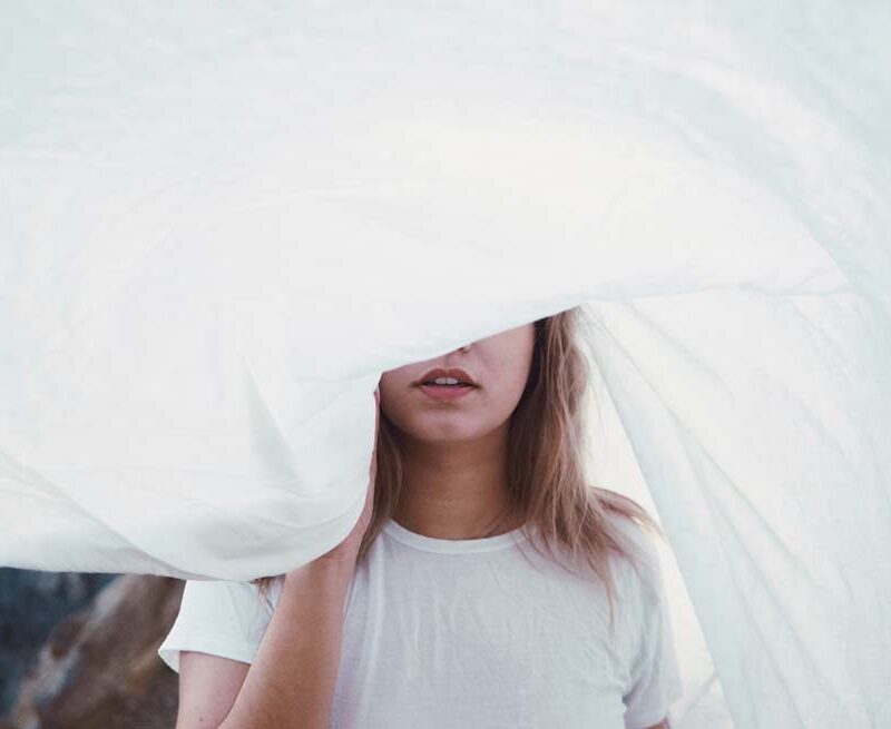 Woman's face partially hidden by white cloth.